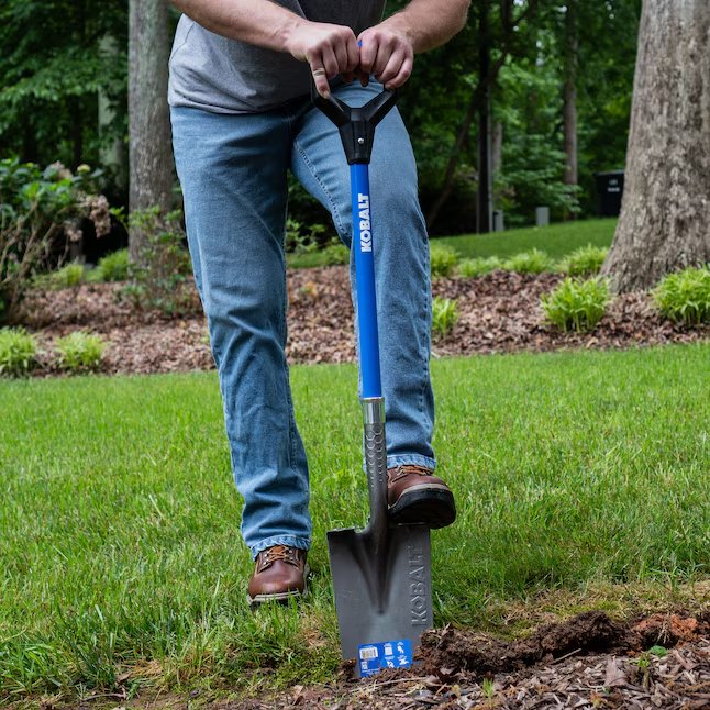 A DIYer using a garden spade to create a new flower bed.