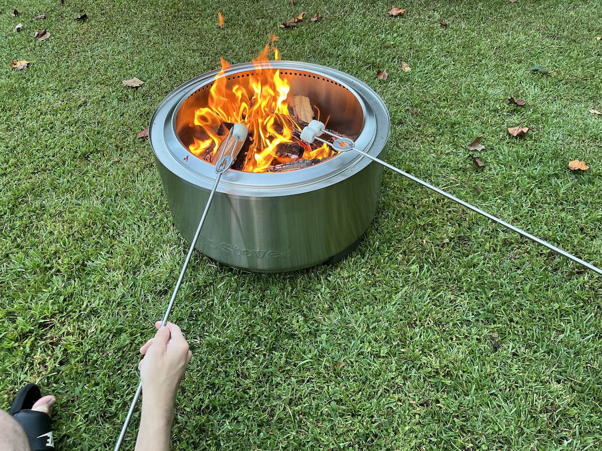 A man and companion roast marshmallows on skewers over the Solo Stove Summit 24