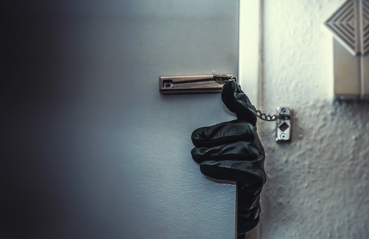 Gloved burglar with crowbar breaking and entering through person's front door and chain door lock.