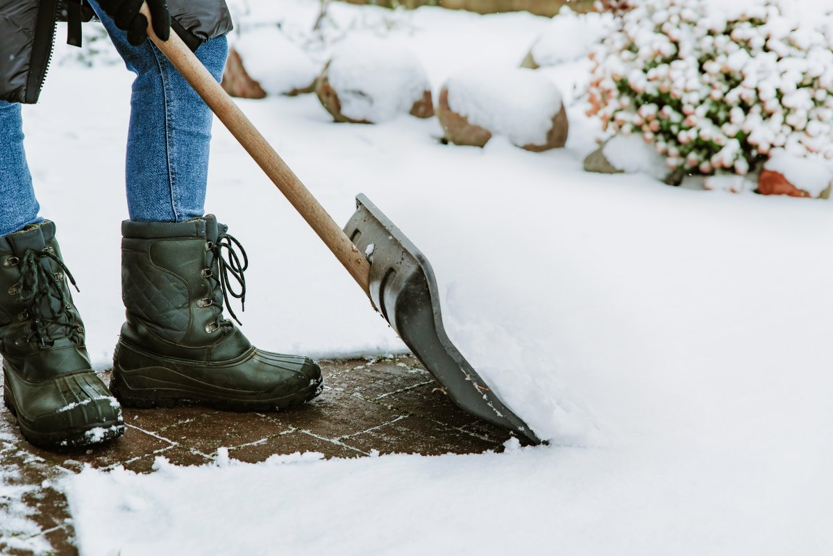 Person in winter boots and clothes cleaning snow outdoors with big winter shovel. Clearing driveway of snow on cold frosty day after snowfall