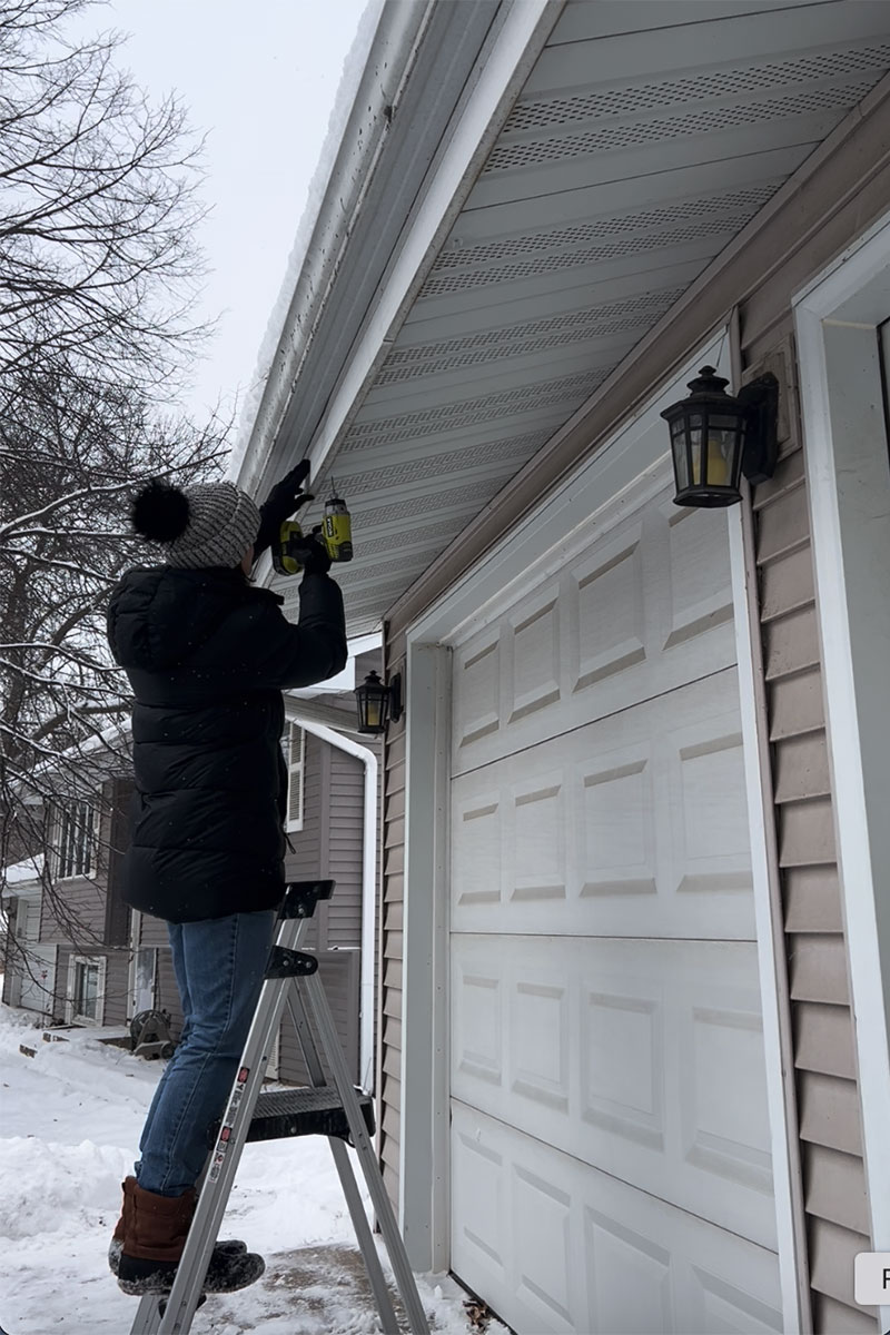 Editor Jenny Stanley installing brackets on house soffit for hanging Christmas lights.
