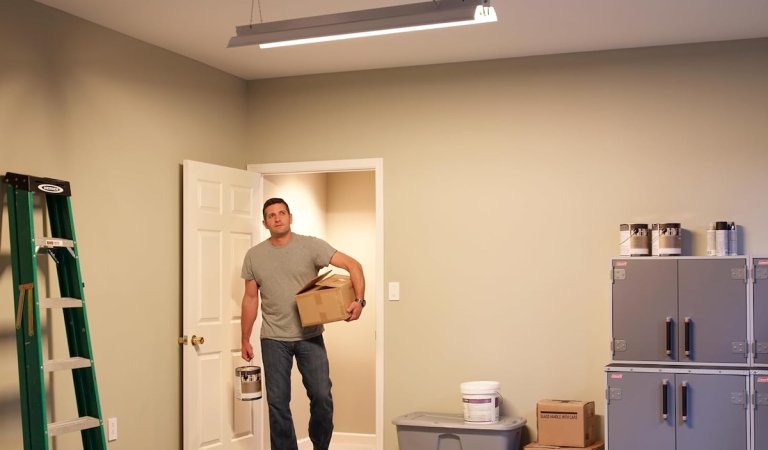Man walking into an illuminated garage with boxes and gear in his hands.