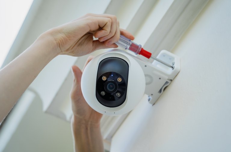 A woman installs a security camera on the facade of a home.