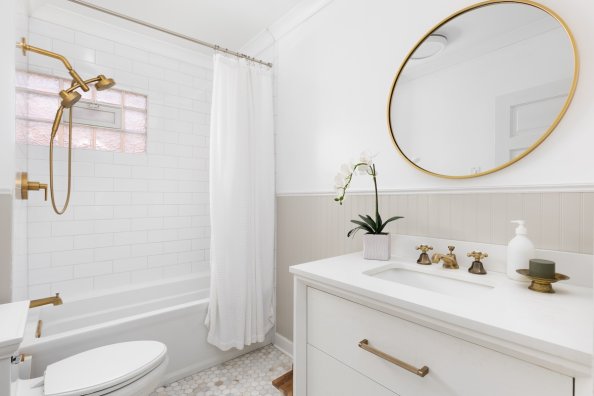 A small bathroom with warm white walls and light gray shiplap. A brass mirror hangs above the vanity.
