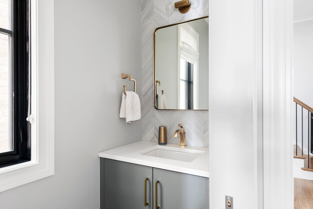 A small bathroom with brass fixtures and a cool, gray paint color.