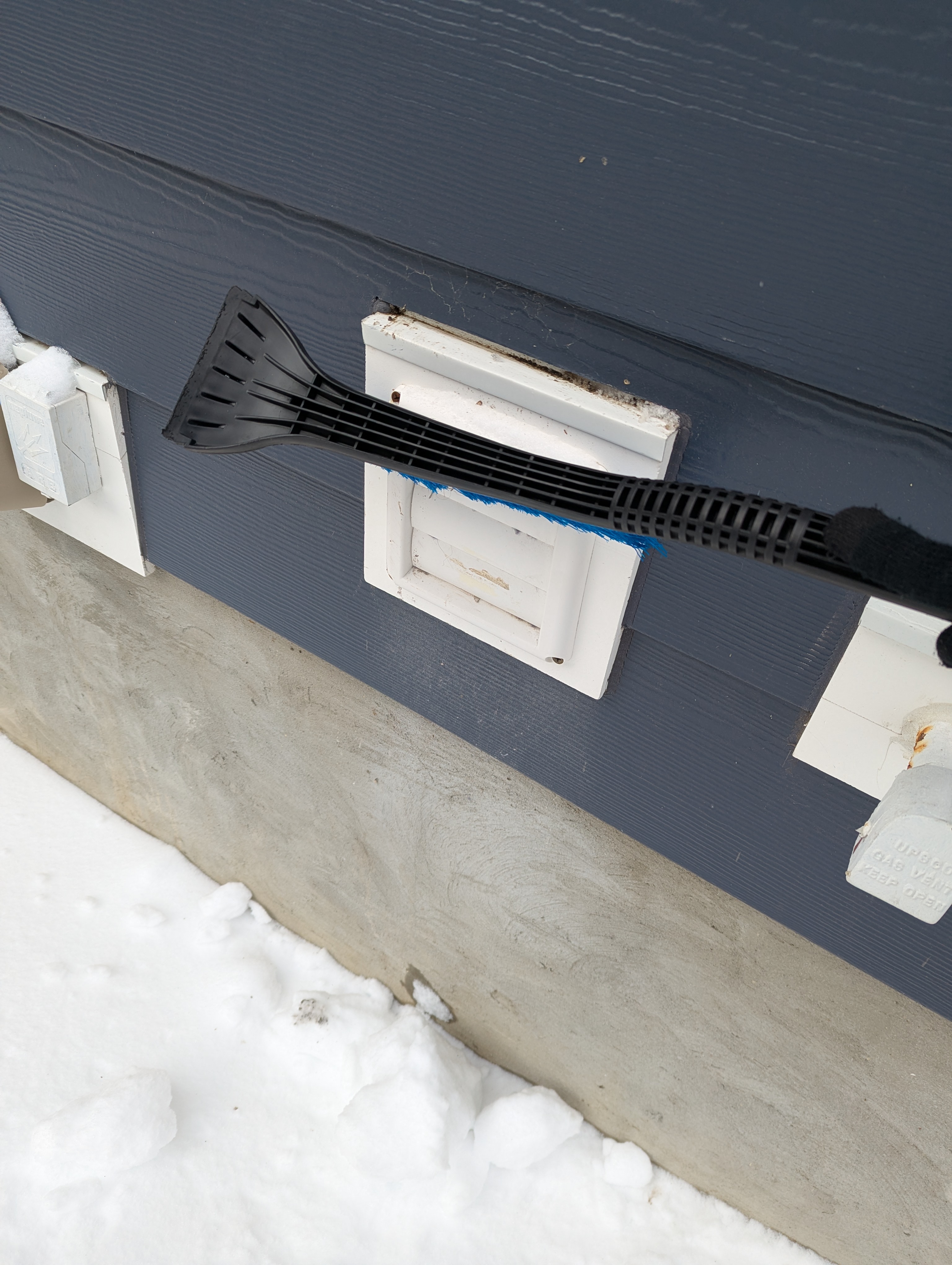 Windshield brush wipes light snow from dryer exhaust vent in winter