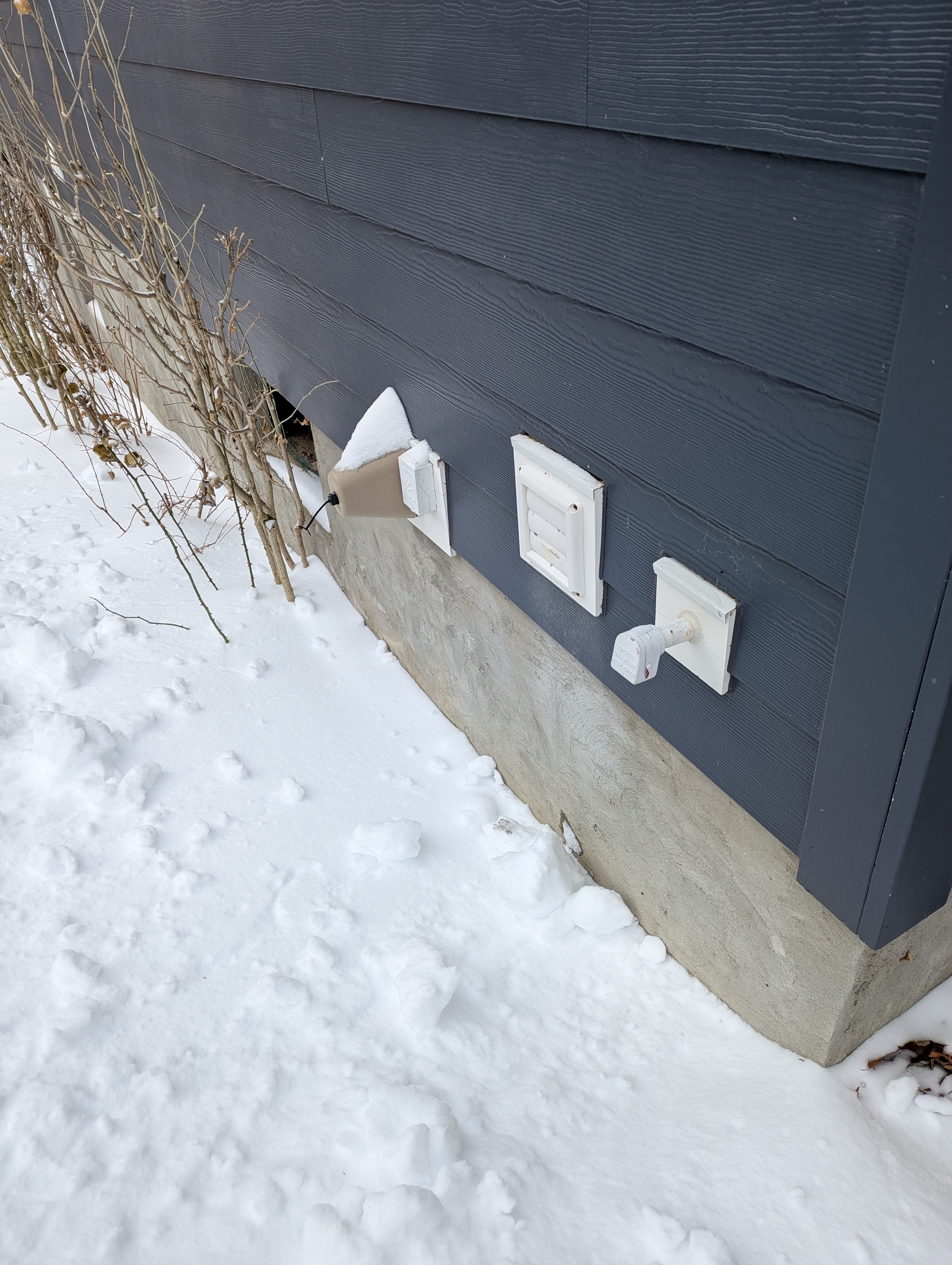 Dryer exhaust vent on a navy home exterior in winter, unclogged even after snowstorm