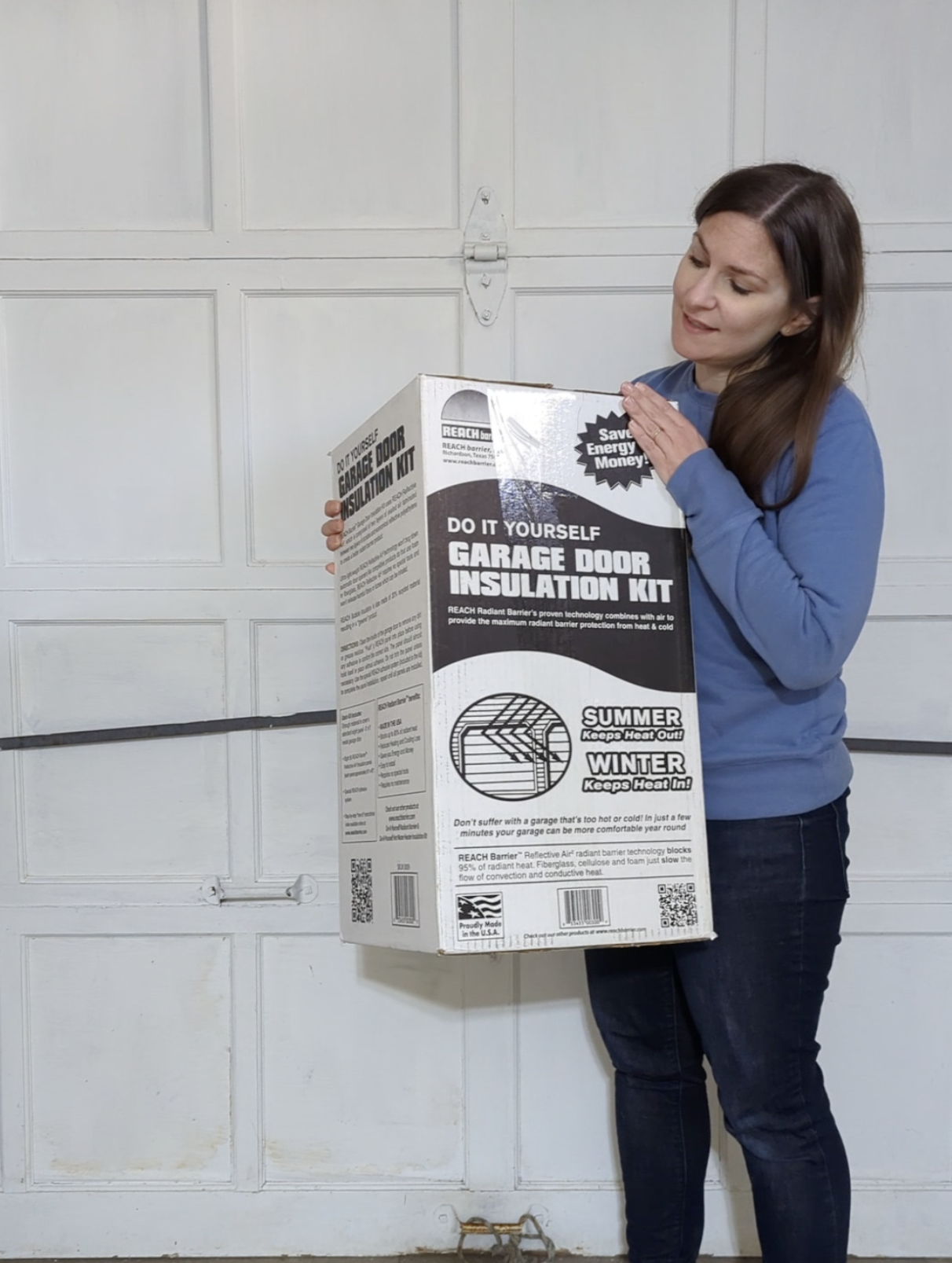 Woman holding the box for the Reach Barrier Garage Door Insulation Kit in front of a painted wood garage door