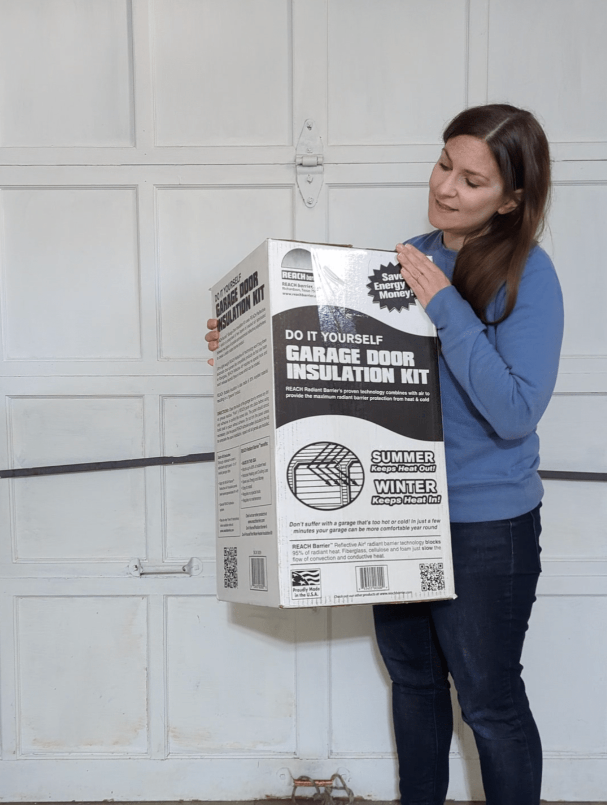 Woman holding the box for the Reach Barrier Garage Door Insulation Kit in front of a painted wood garage door