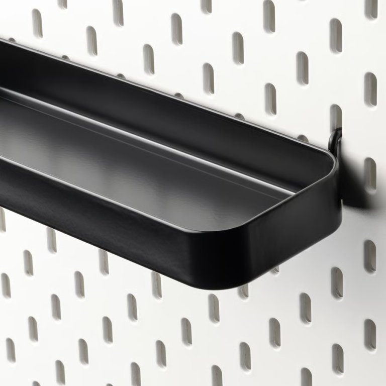 Ikea Skadis black shelf hanging on a white pegboard