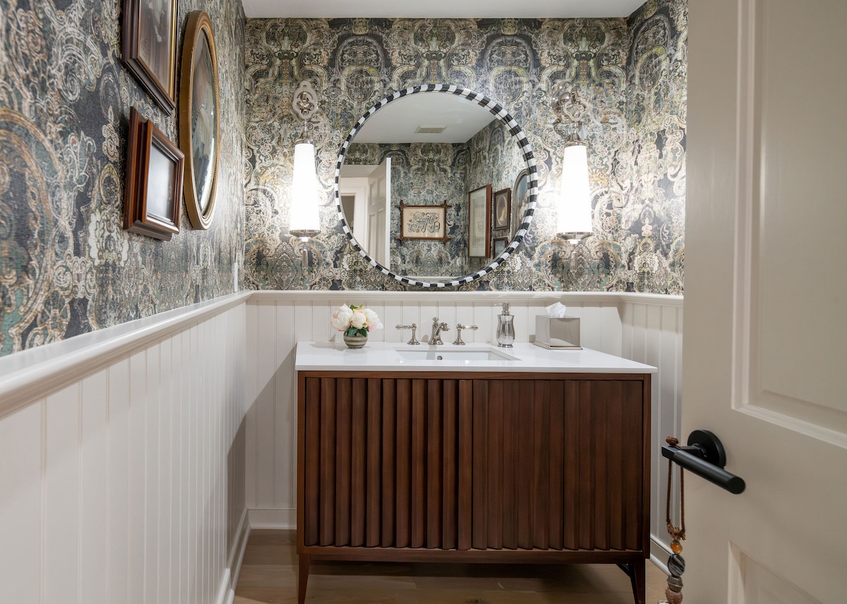 A small bathroom with ornate wallpaper and shiplap painted in a cool, white shade. 