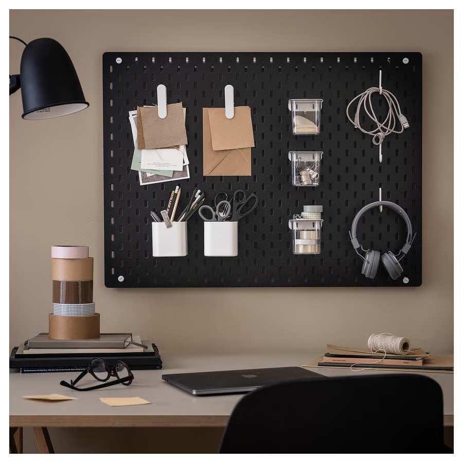 Ikea Skadis black pegboard used in an office setting to move materials off of the desk, including cords, headphones, pens, and memos