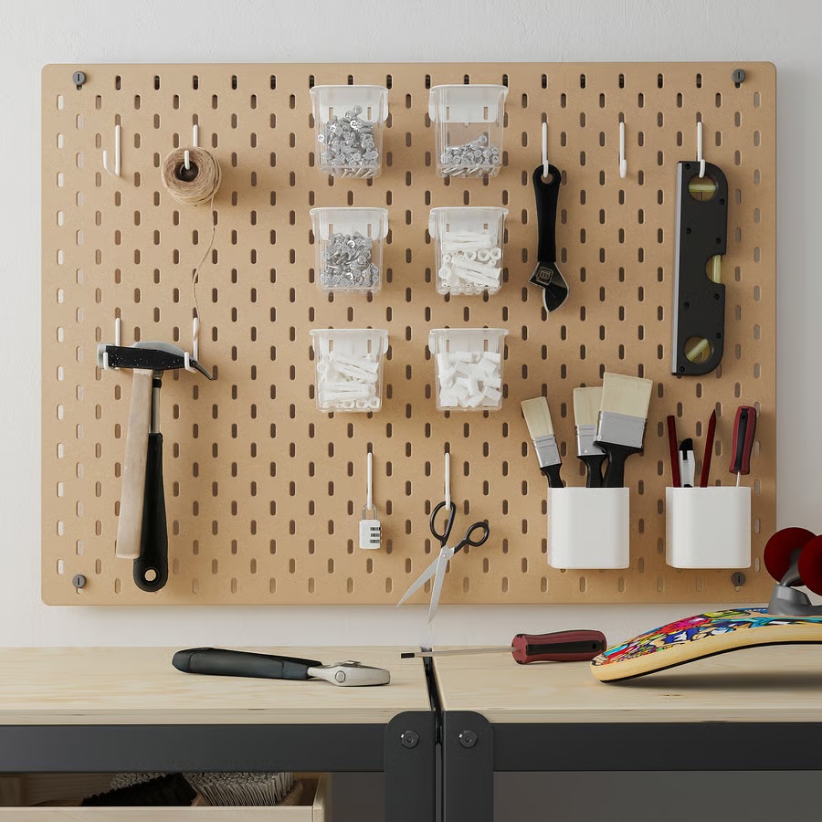 Ikea Skadis wood pegboard used in a workshop setting to hang small tools, like scissors, hammers, levels, fasteners, and more behind a worktop