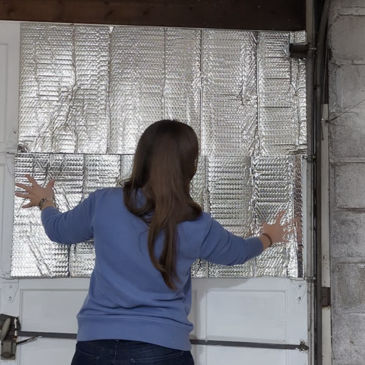 Woman sticking up reflective Reach Barrier insulation panels on the interior of a painted wood garage door