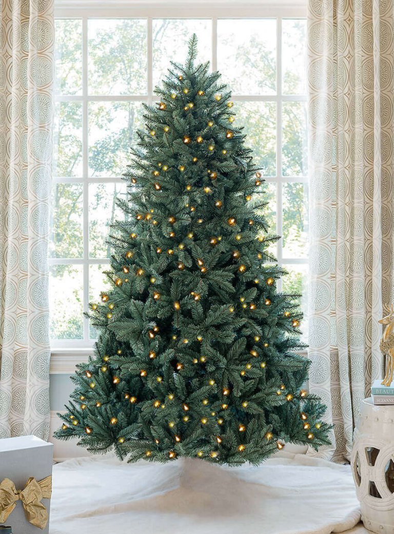 An artificial Christmas tree in front of a sunny window in a home.