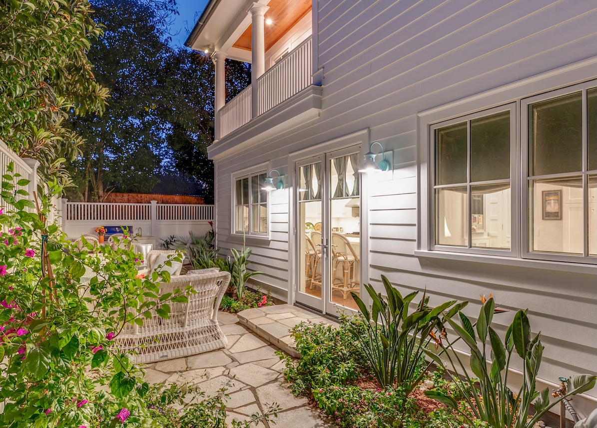 Beautiful backyard garden with patio table illuminated by two gooseneck lights near the patio doors.
