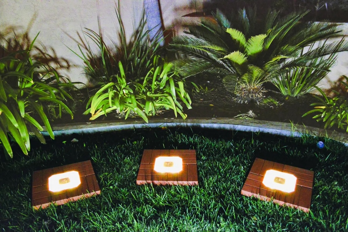 Three Homebrite Solar wood solar stepping stones with integrated LED lights, in a garden scene.