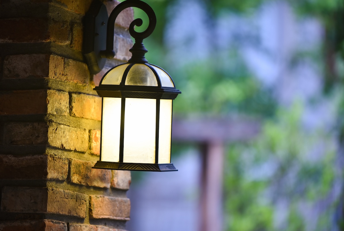Illuminated hanging vintage lantern sconce hanging from a brick building at dusk. 