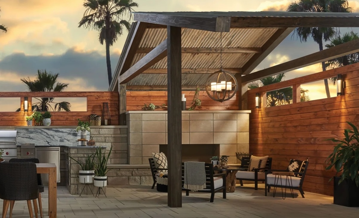Outdoor scene of large dining table, and patio set under an awning, lit at dusk with an outdoor chandelier and sconce lighting.