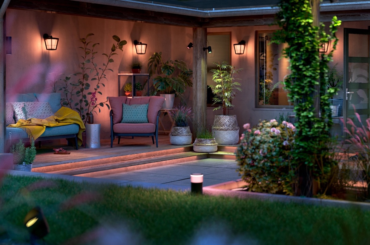 Outdoor patio with sconces on stucco walls and landscaping around, all bathed in colored outdoor lighting.