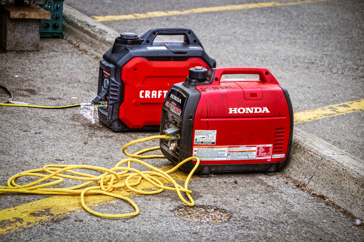 Two red and black portable generators are attached to a long, yellow extension cord.