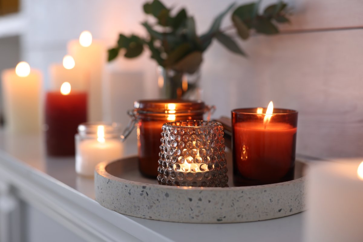 Burning orange and cream candles on mantel near white wall indoors.