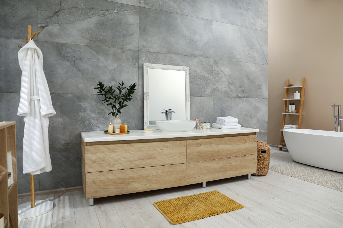 Modern light wood leg-style bathroom vanity with vessel sink, toiletries and mirror on vanity.
