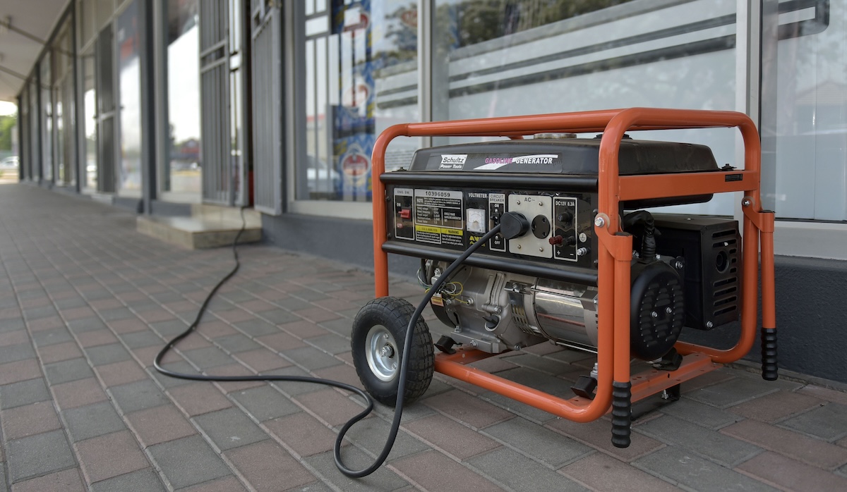 A small, orange portable generator is plugged into an outdoor corridor.