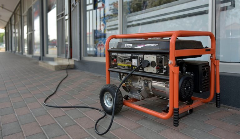 A small, orange portable generator is plugged into an outdoor corridor.