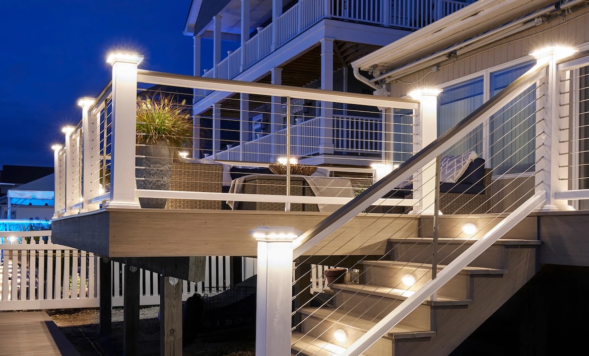 Home exterior deck with illuminated white wood posts, step lights, and cable railings.