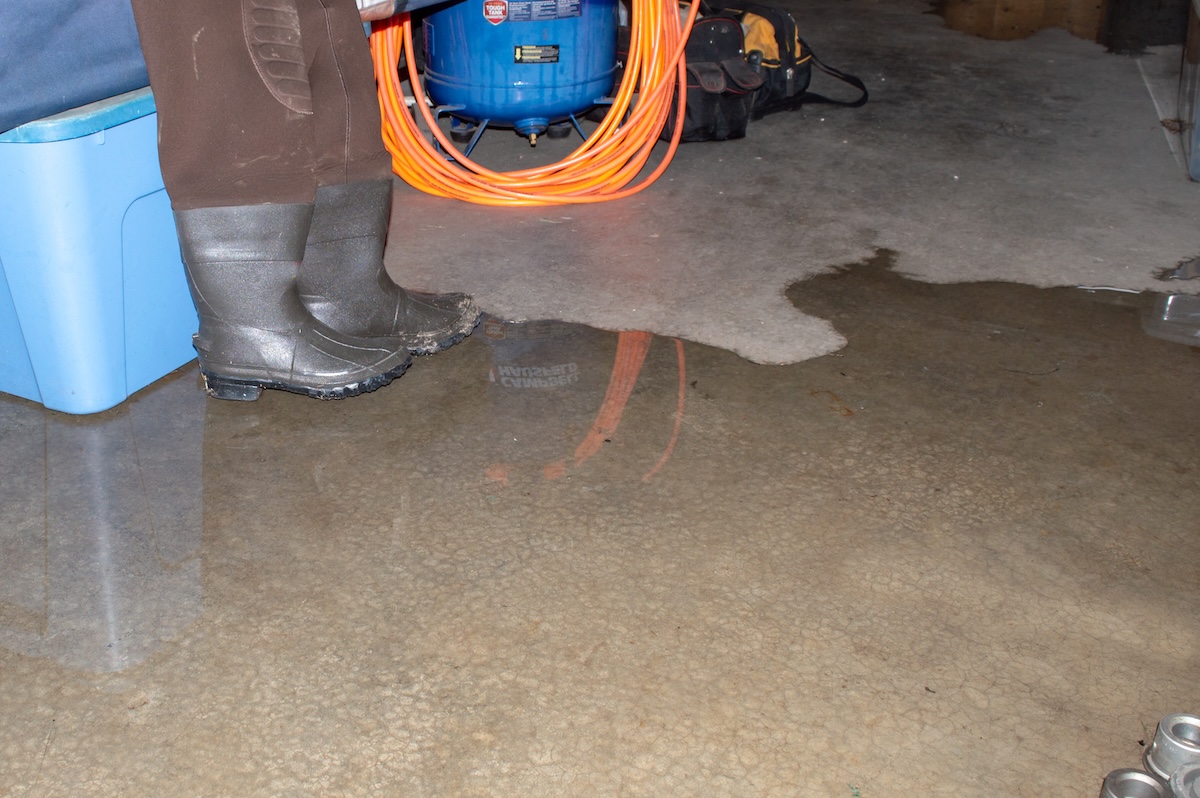 A homeowner standing in a wet basement with water pooling on the floor and tools and supplies on the floor.