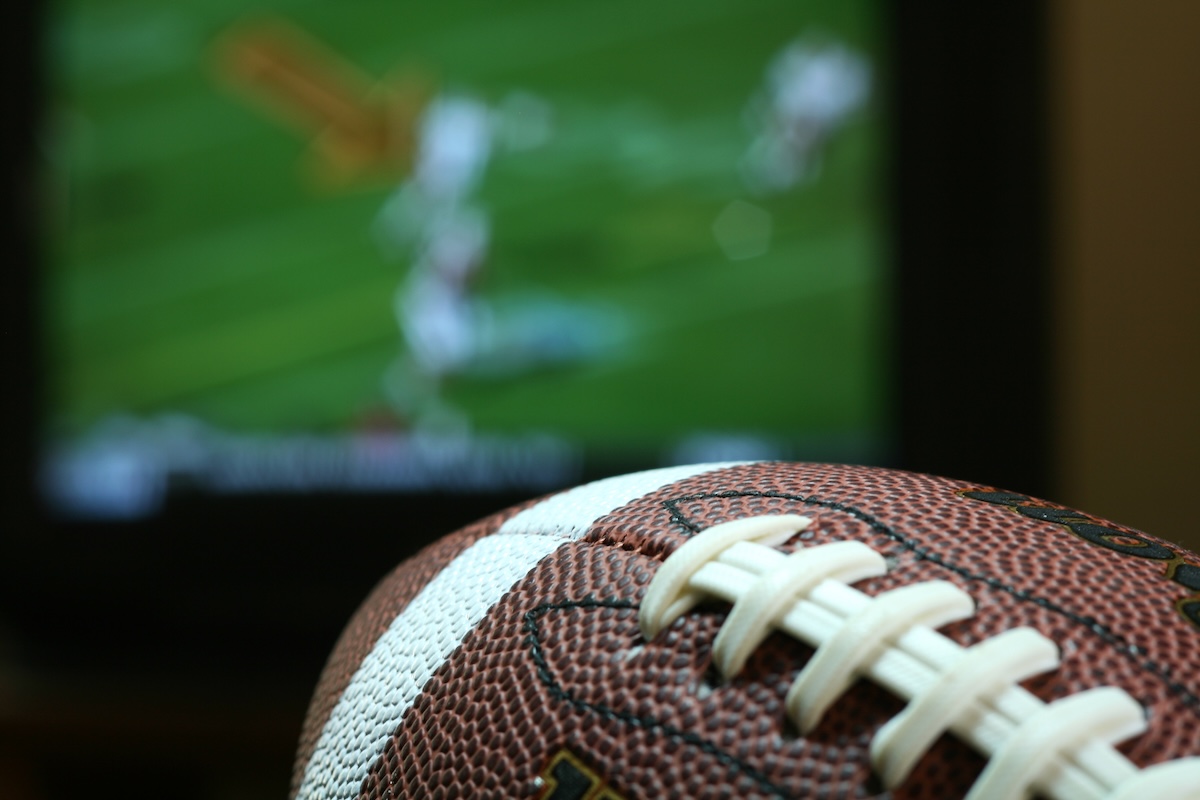 A football game on a TV with a football in the foreground.