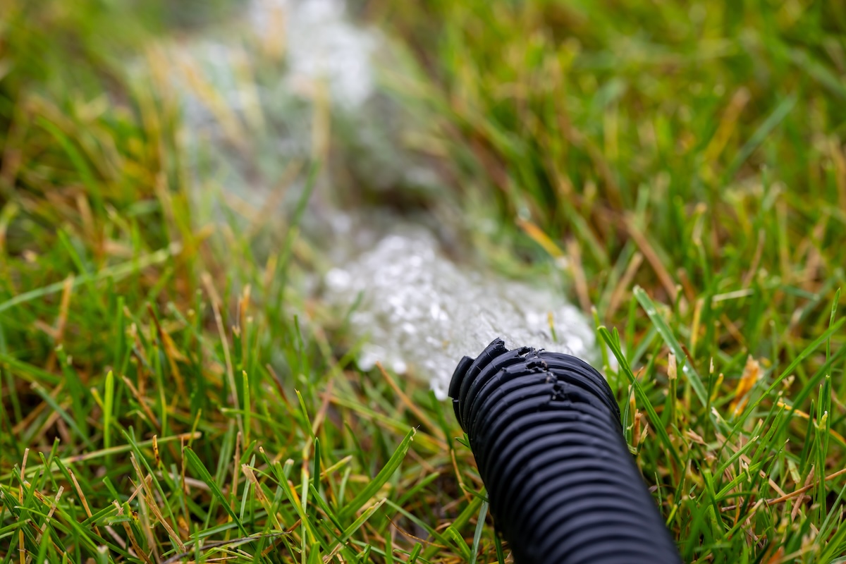 A sump pump downspout directing water away from a home foundation.