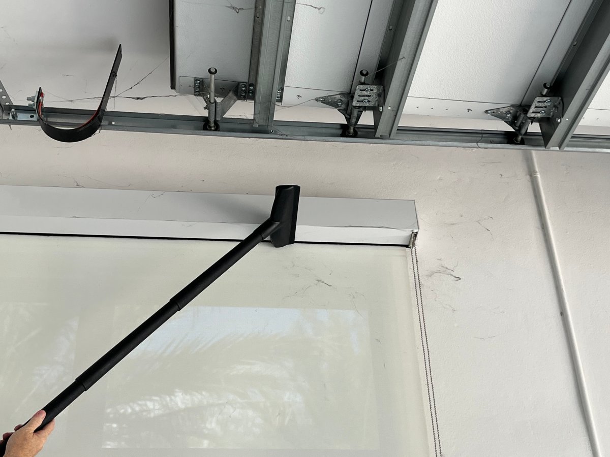 Hand holding the vacuum brush attachment to reach the sealer spider webs on the garage window shade.