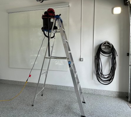 Vacuum with attachments tied to the highest step of a ladder with a bungee cord.