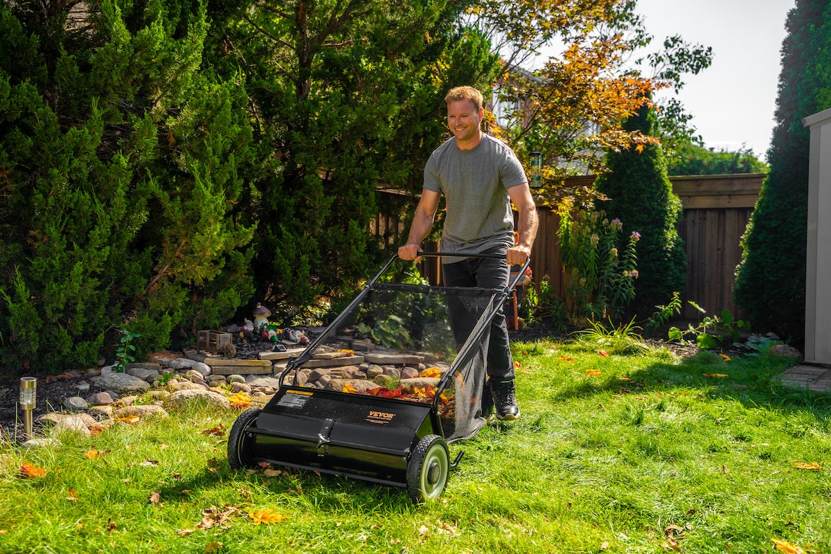 A DIYer using a lawn sweeper to clean up debris from a yard.