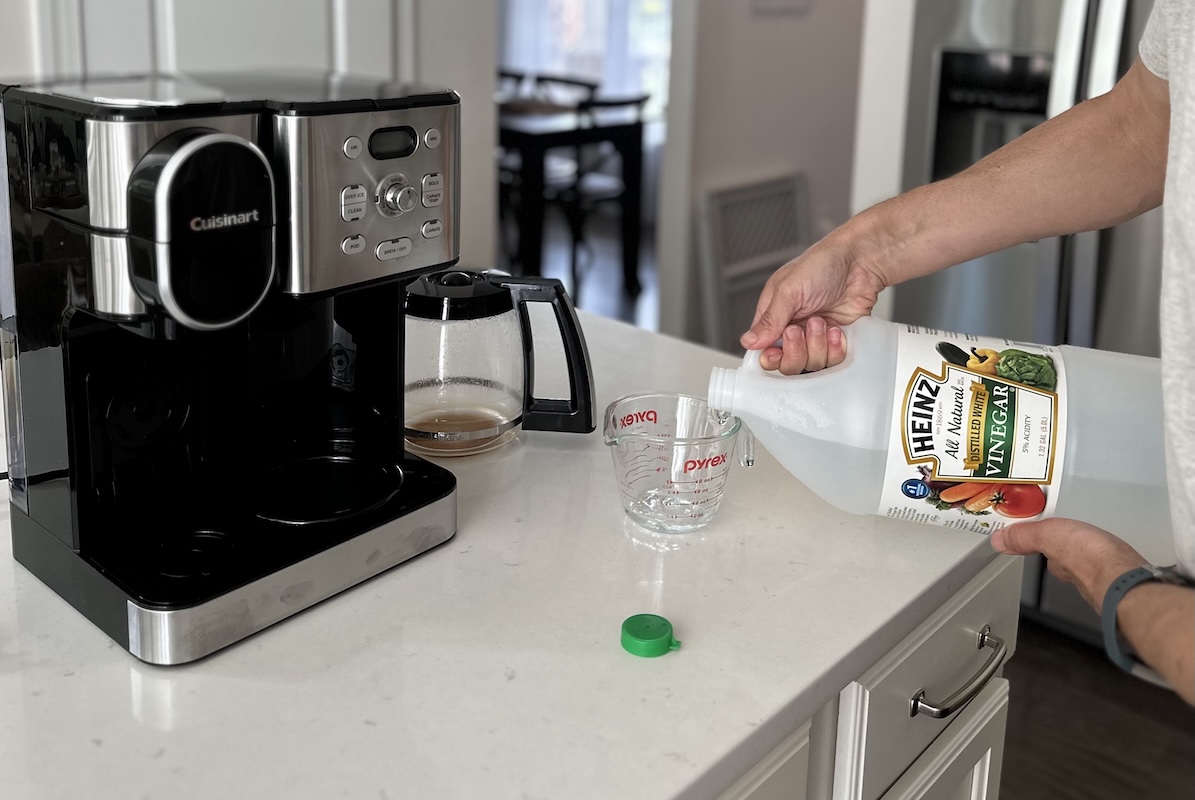 Man pours vinegar into a measuring cup from a gallon jug, a Cuisinart coffee maker sitting nearby.