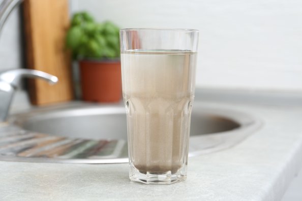 Glass with dirty water near kitchen sink faucet.