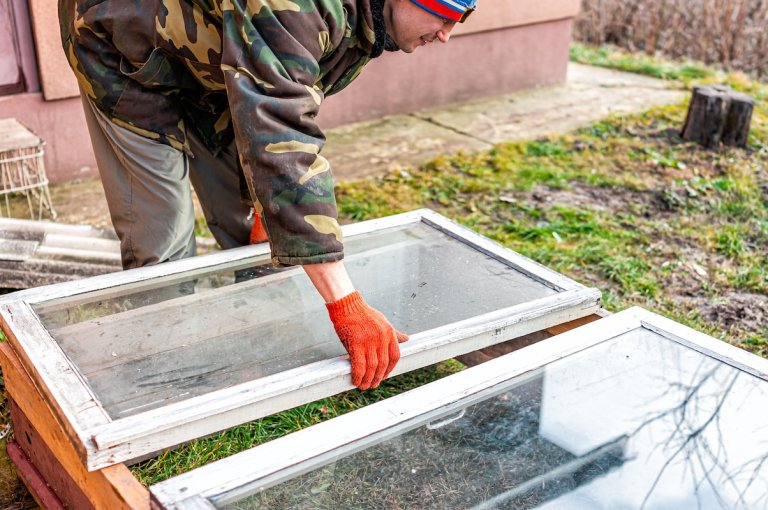 Man placing top window on DIY cold frame outdoors in winter.