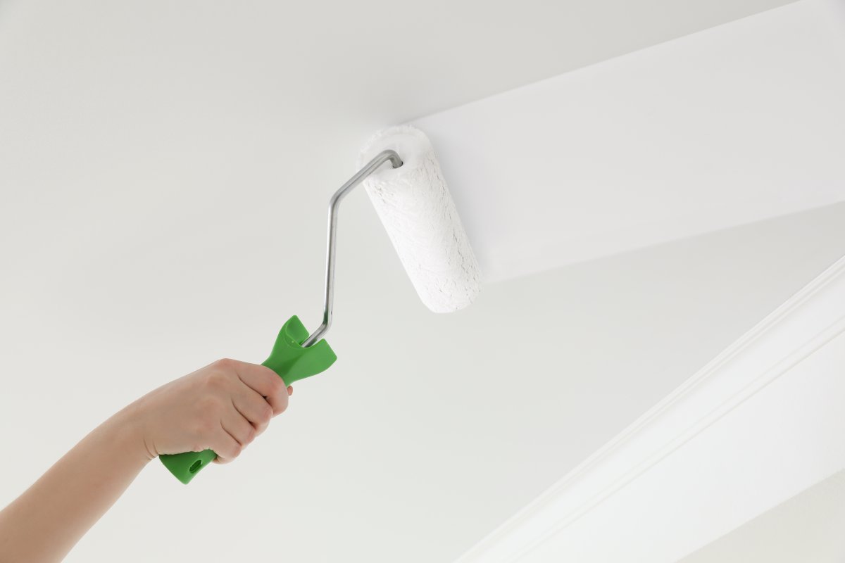 Hand painting a ceiling white using a roller.