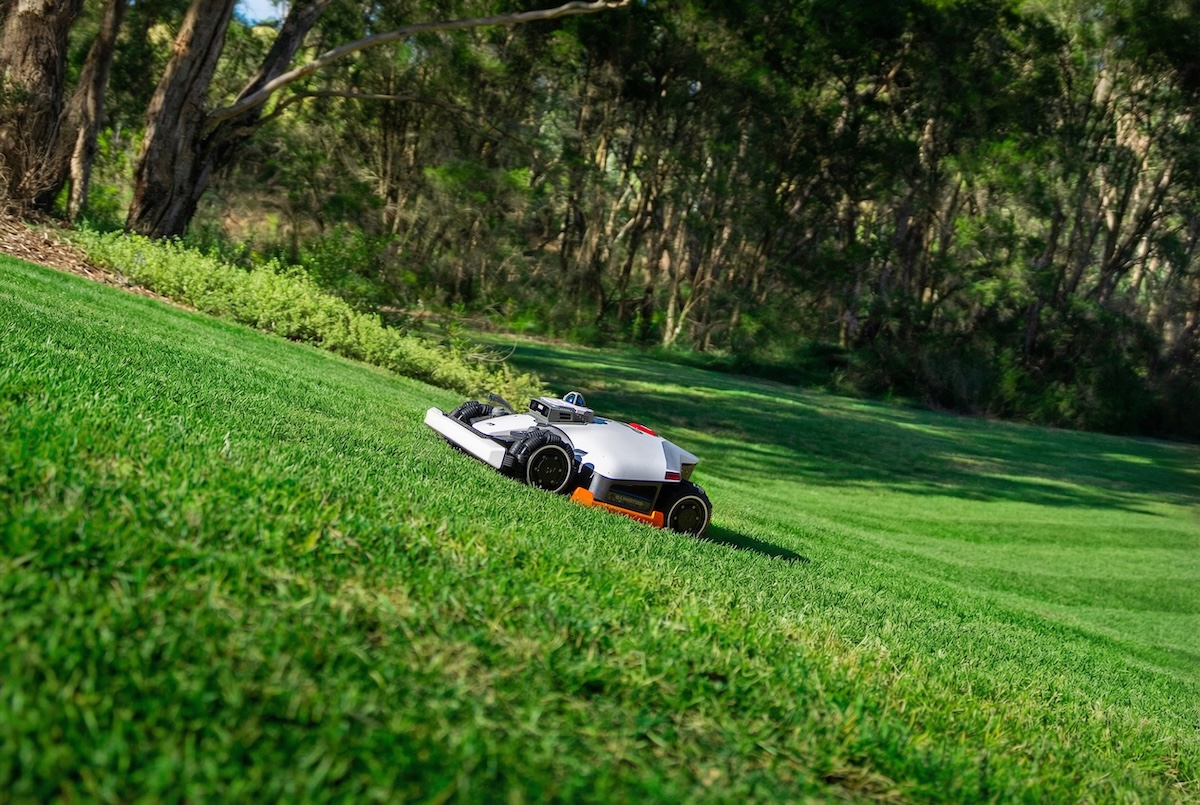 A Mammotion robot mower climbing a hilly backyard to mow the grass.
