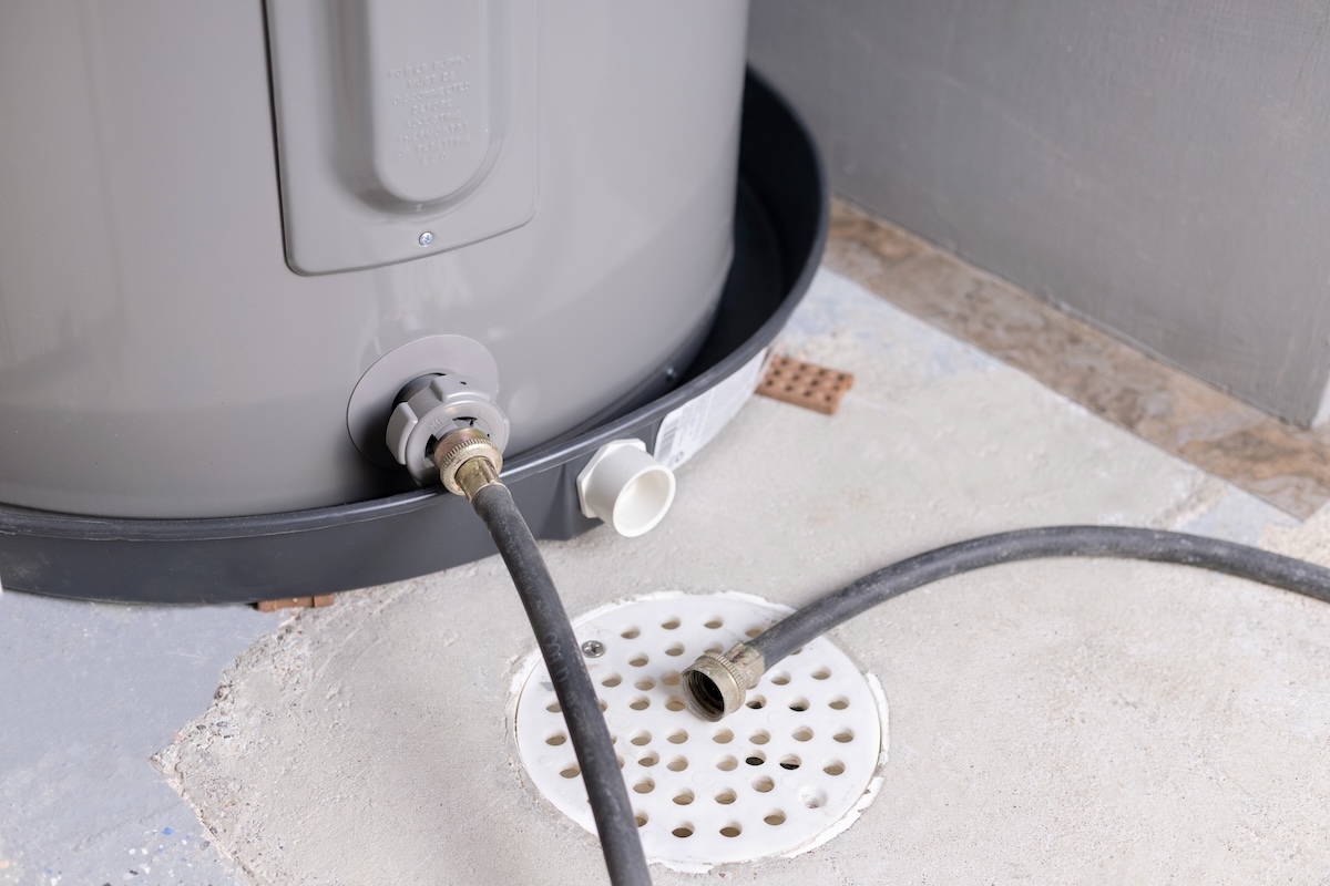 A hose connected to base of a water heater feeds into a drain in a basement floor.
