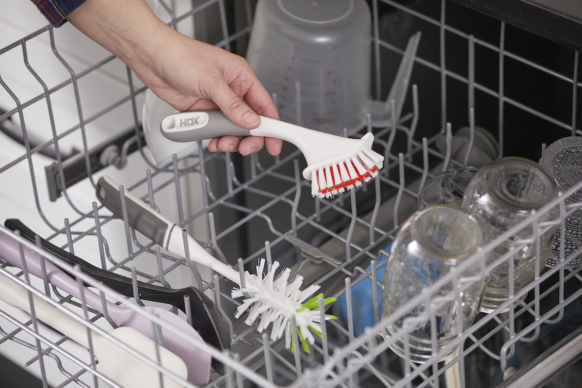 Woman places small scrub brushes in top rack of dishwasher for cleaning.