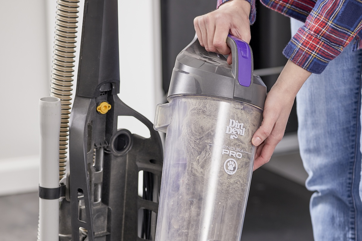 Woman empties a vacuum canister full of dust and debris.