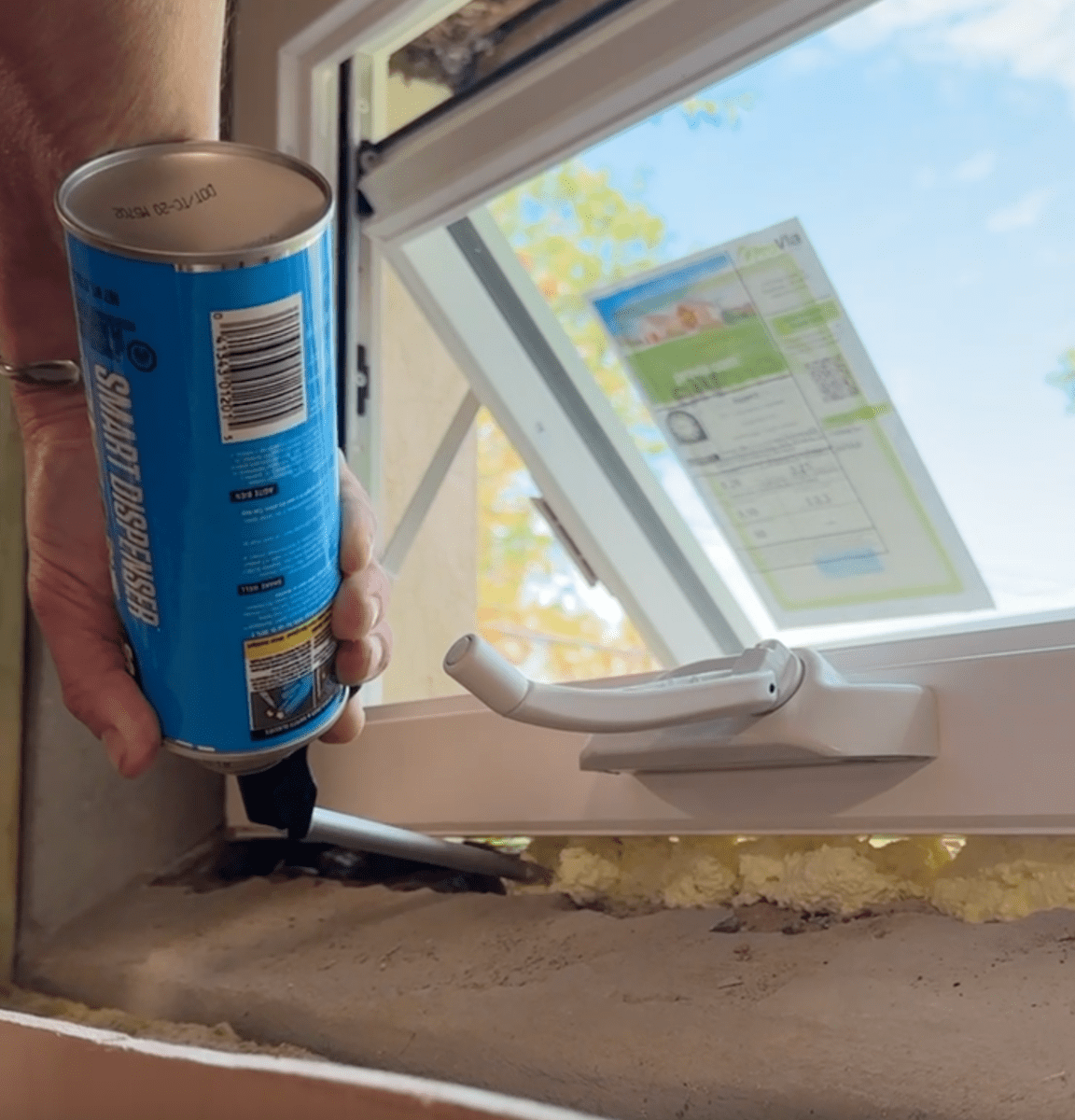 Applying expanding foam to insulate around basement window.