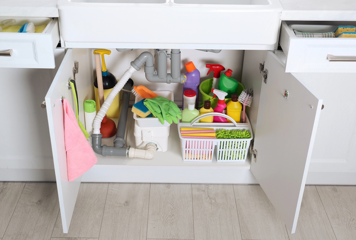 Open under sink cabinet with different cleaning supplies in kitchen