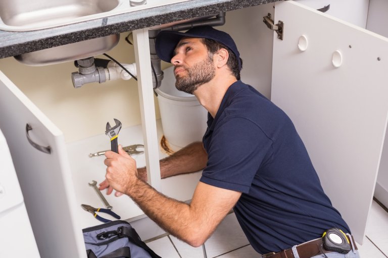 Plumber fixing under the sink in the kitchen