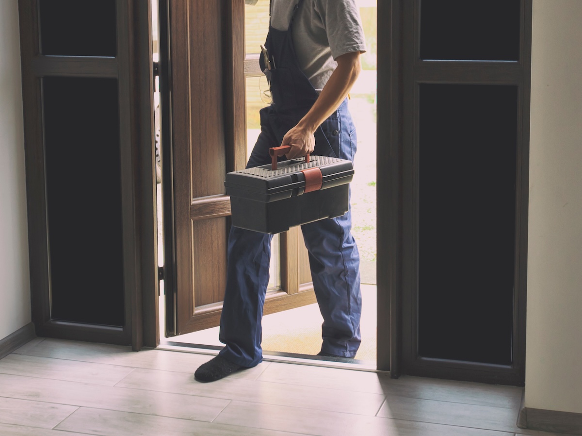 The repairman plumber enters the house with toolbox in his hand.