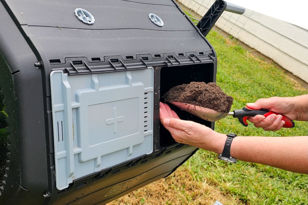 A person scoops fresh compost out of a compost tumbler using a trowel.