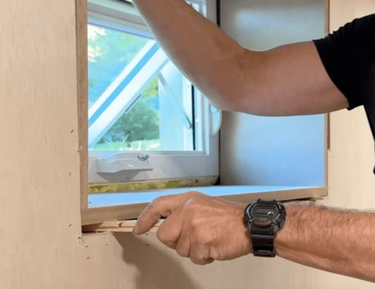 Shimming a basement window box in place for trimming basement windows.